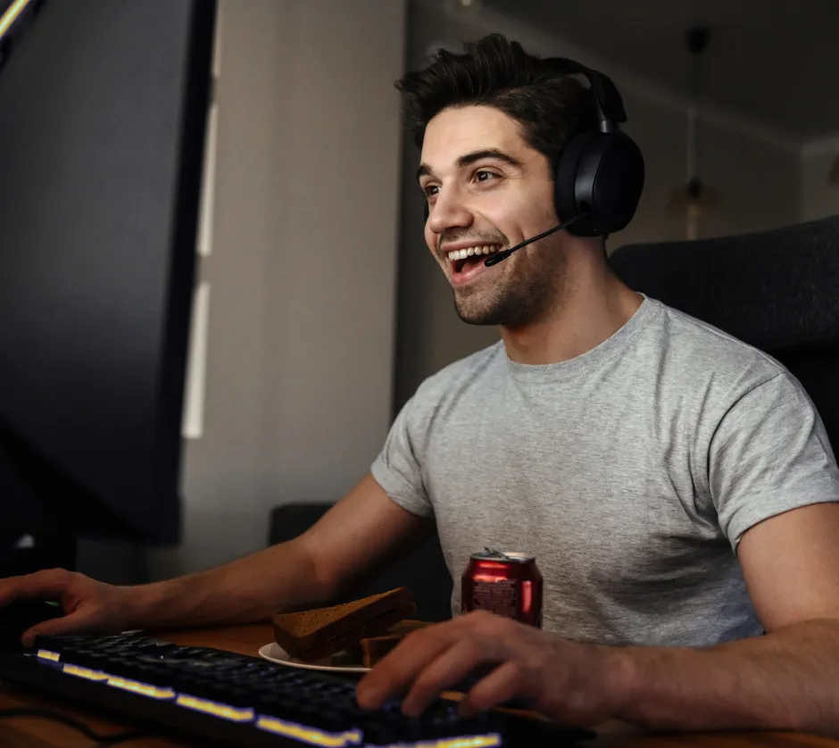 White caucasian man with headphones smilling and playing a game on his computer