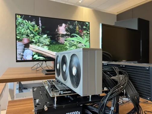 A GPU on a test bench with a monitor showing Evolve Benchmark in the background.